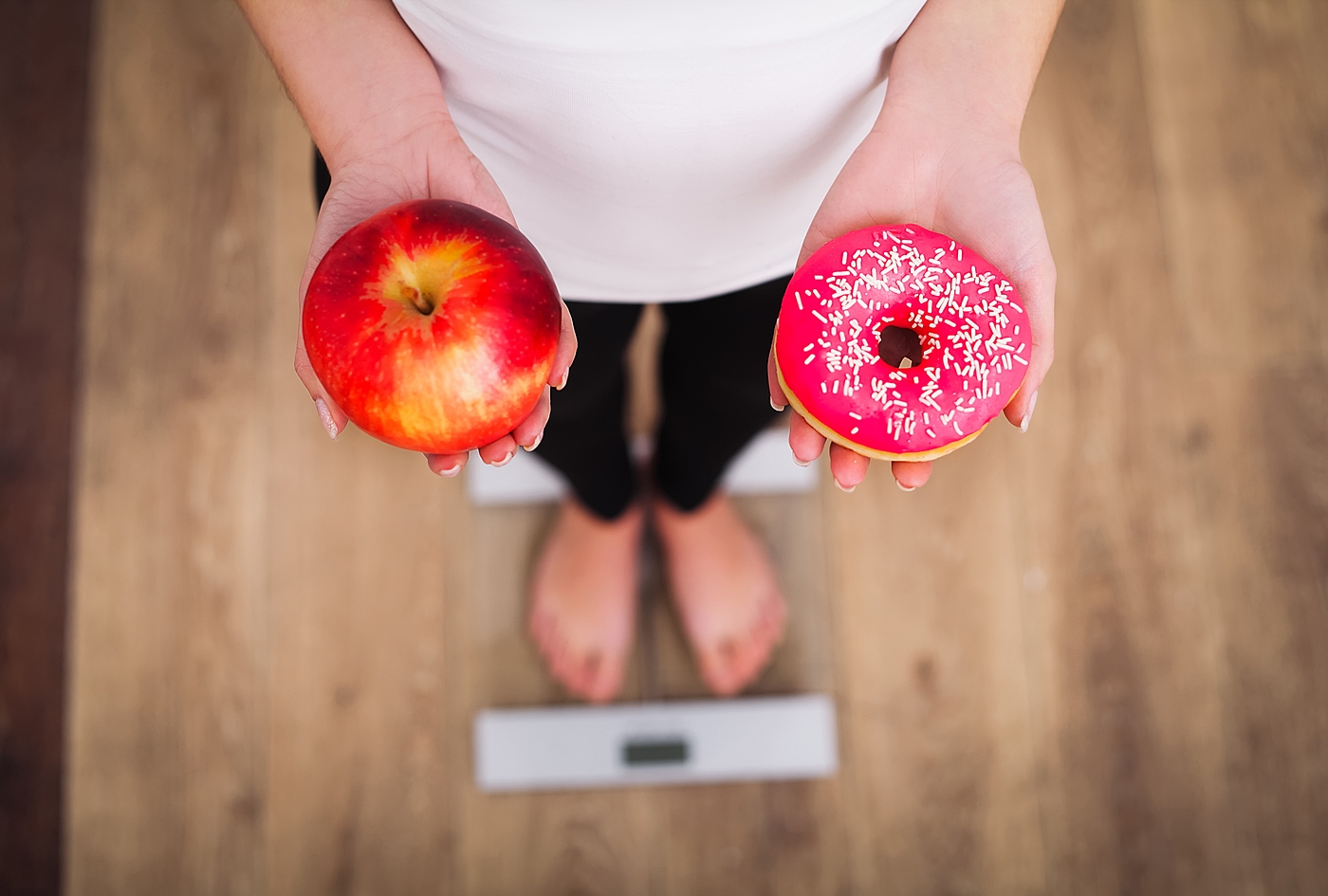 体重計に乗って果物とドーナツを比べる女性